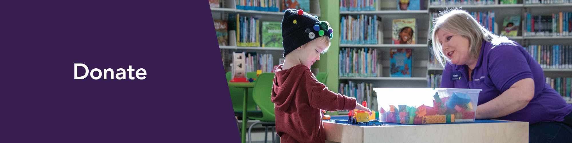 DESIGN-HEADER-banner-donate Donate - A friendly staff member plays a game on an interactive screen with a child