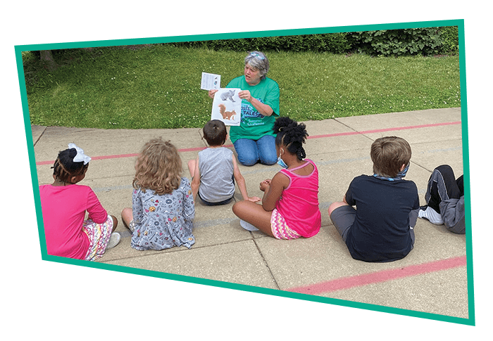 A friendly staff member reads to a group of children outside